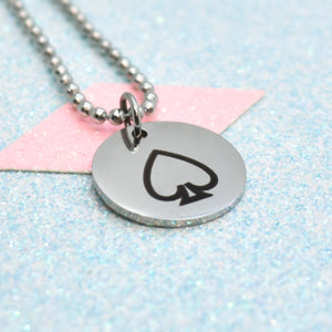 The image shows a silver-coloured necklace with a pendant featuring a black asexual emblem. The pendant is round and has a shiny, metallic finish.