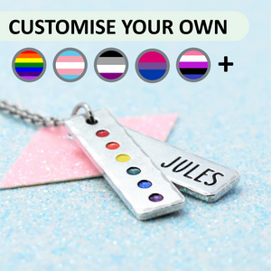 Customisable lgbtq pride pendant with rainbow pride colours and 'JULES' engraved, on a light blue background.