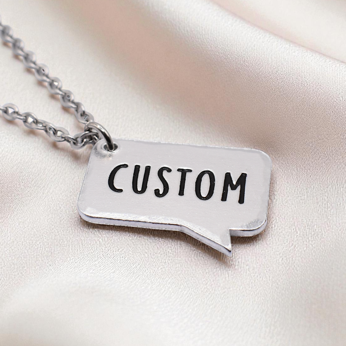 Silver necklace with a pendant labeled 'CUSTOM' on a satin surface