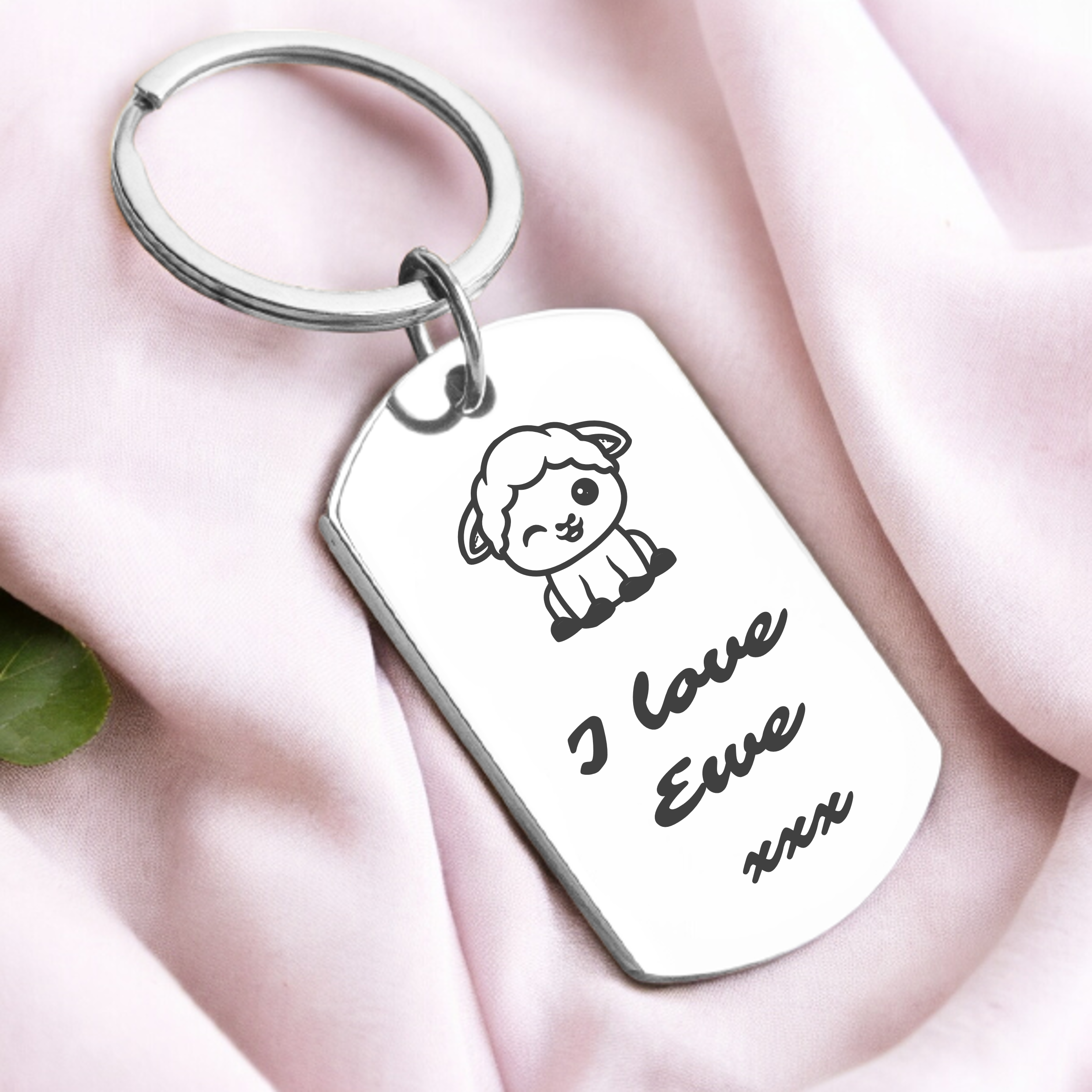 A personalized key ring with a sheep design and the phrase 'I love ewe' engraved on it, presented on a pink fabric surface.