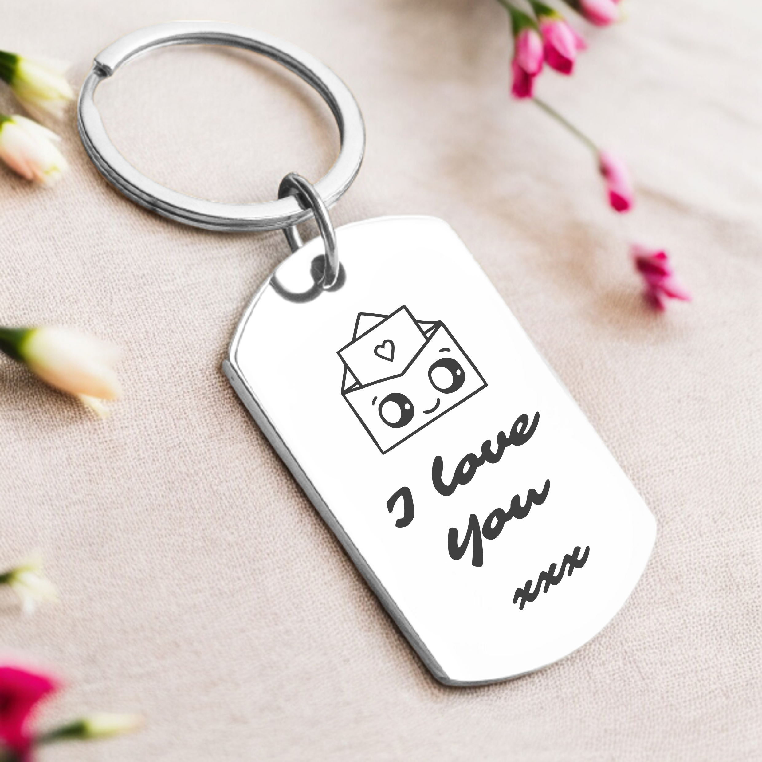 A personalized key ring with a silver or gold finish, featuring the phrase 'I love you' along with a personal message, presented in a box with flowers in the background.