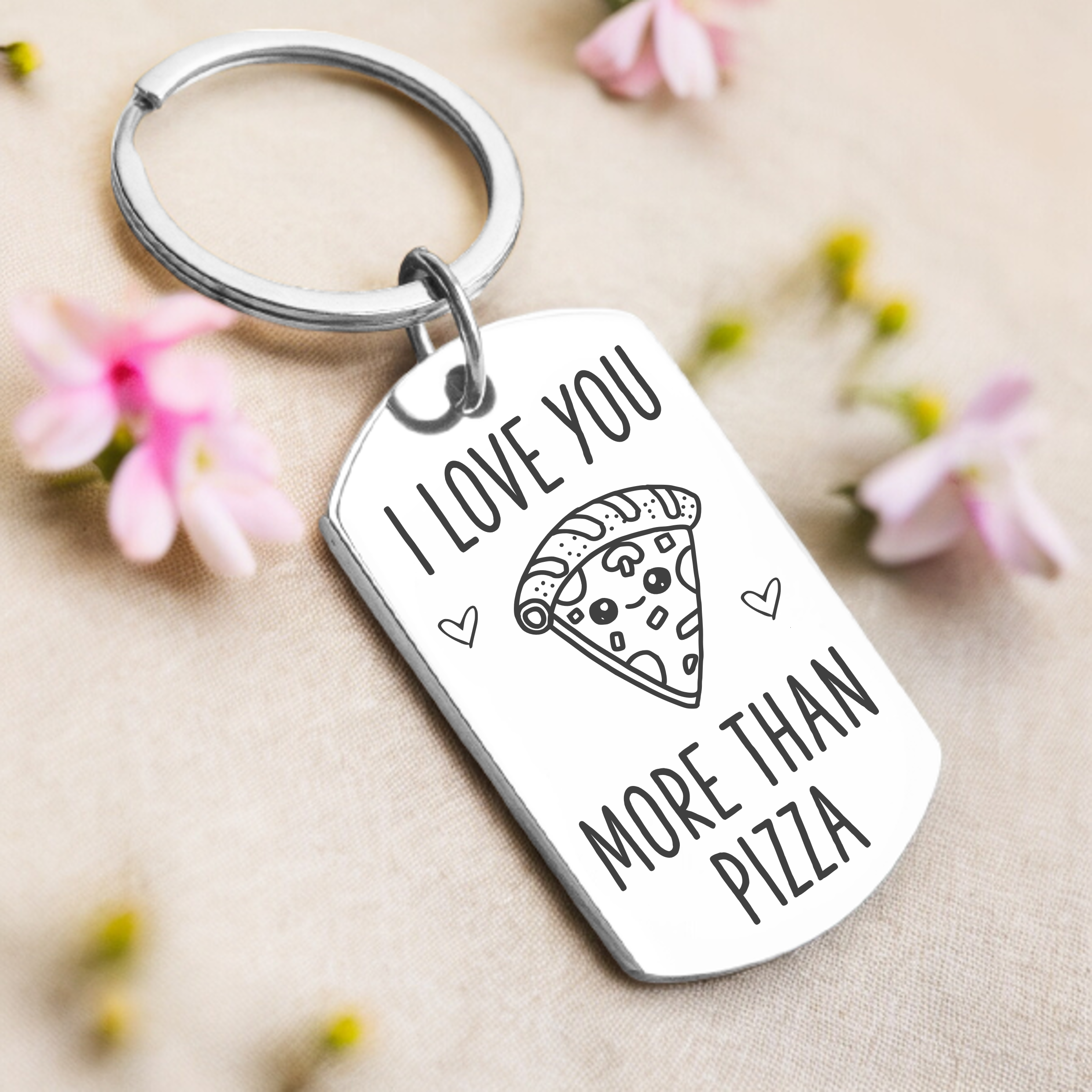 A key ring with a rectangular tag featuring the text 'I love you more than pizza' and a pizza slice illustration. The tag appears to be made of silver with a mirrored finish, and the key ring is attached to the top loop of the tag.