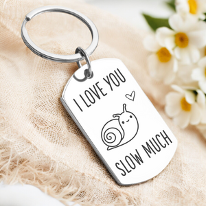A key ring with a rectangular tag featuring a snail illustration and the phrase 'I LOVE YOU SLOW MUCH'. The tag has a high quality mirrored finish and is attached to a silver or gold key ring.