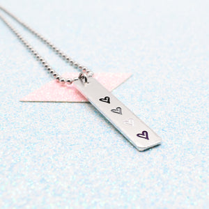 Necklace with a bar pendant on a ball chain featuring colourful hearts representing the asexual pride flag on a light blue background