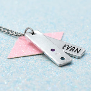 A personalized gender queer necklace with a silver-colored pendant featuring the name 'Evan' on a pink and purple background, attached to a blue cable chain.