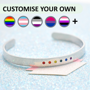 A bracelet with minimalist design, featuring colourful gay pride accents, displayed on a glittery blue background.