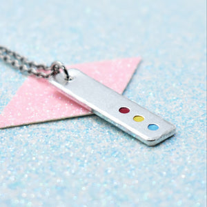 A minimalist pride necklace with a geometric shaped pendant featuring the pansexual flag colours, attached to a silver chain.