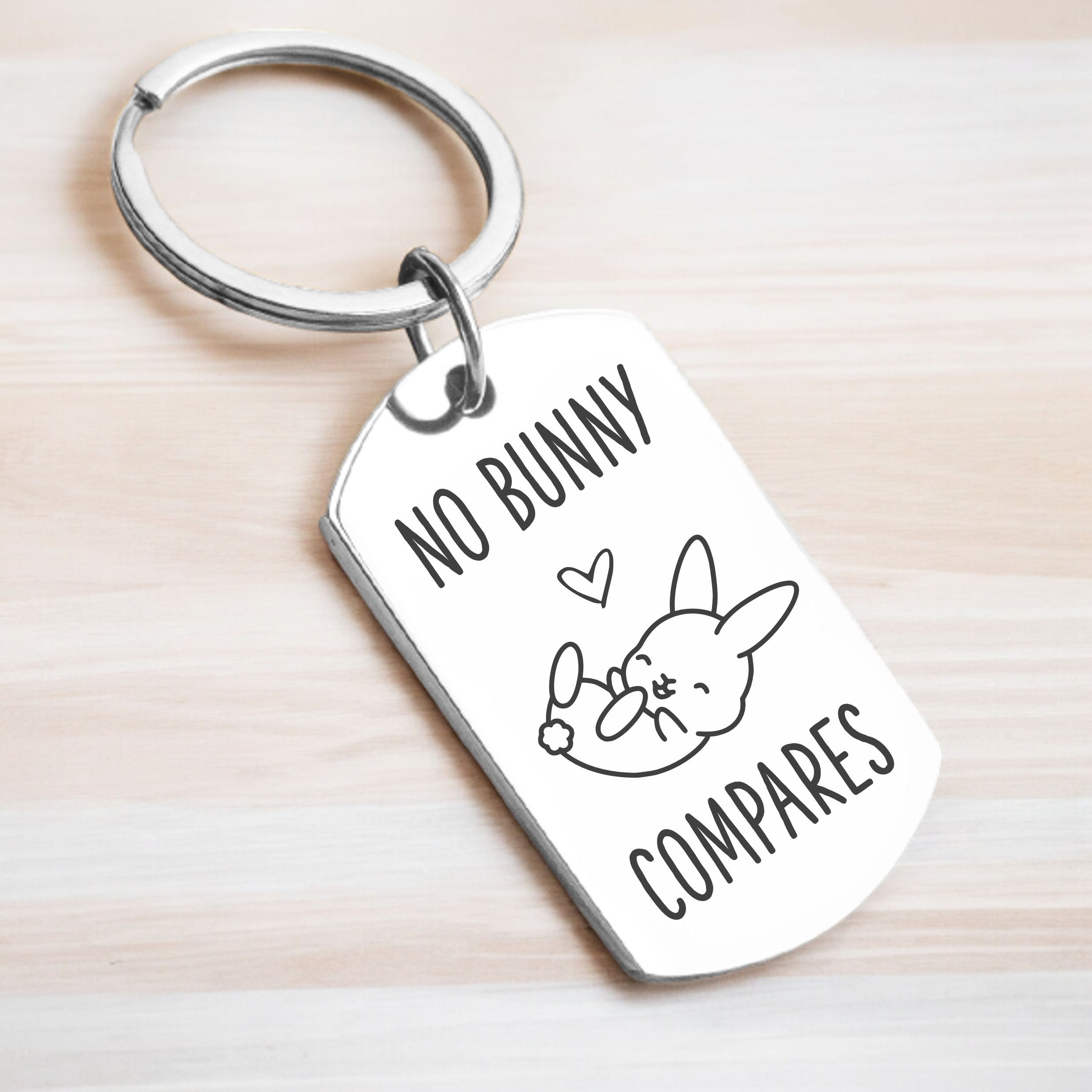A key ring with a rectangular tag featuring text and a cartoon rabbit design, on a wooden surface.