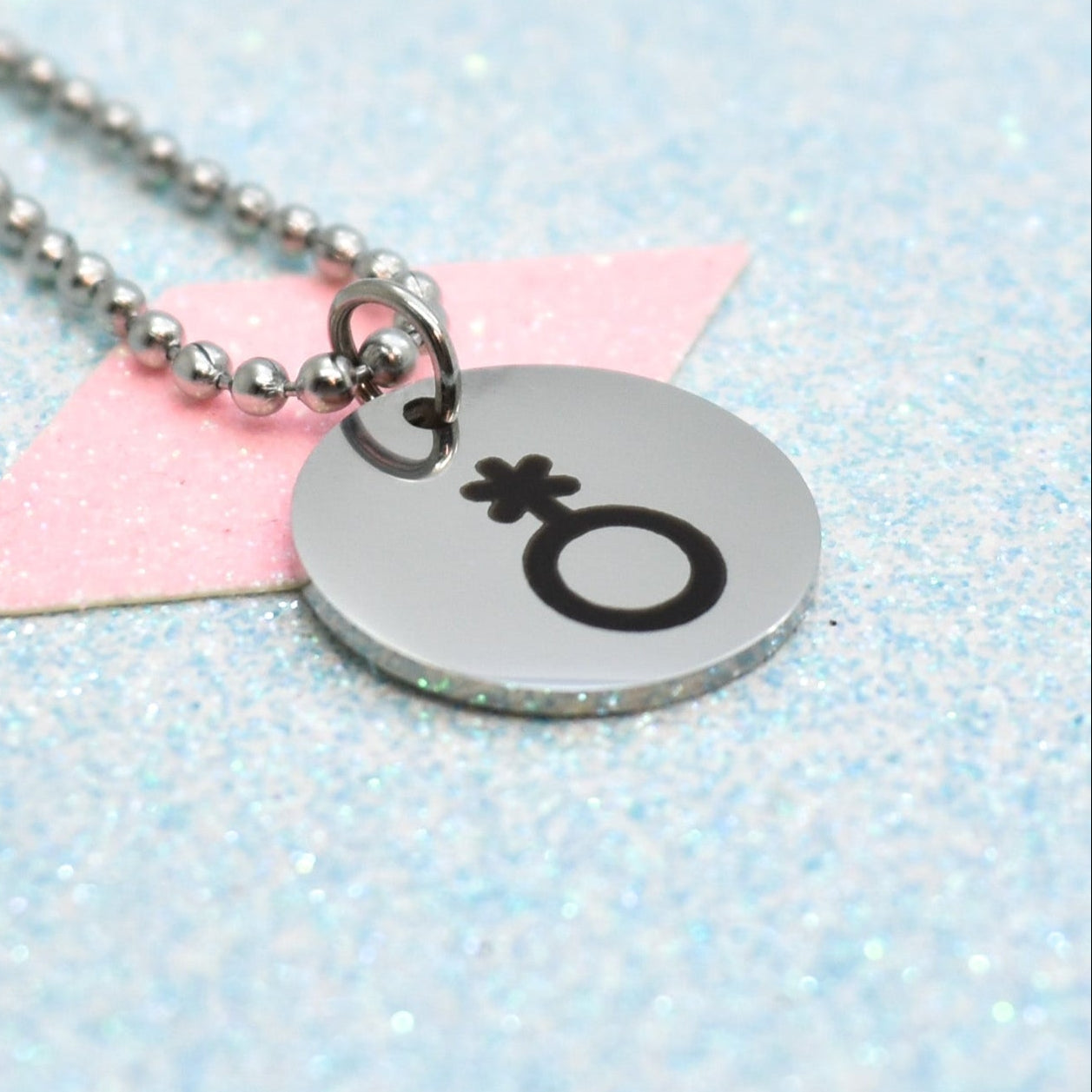 Necklace with a round silver pendant featuring a non binary symbol on a light blue and pink background