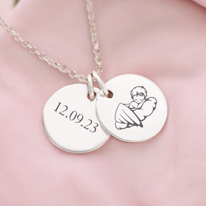 A personalised memorial necklace with two round discs, one engraved with a name or date and the other with an image of a baby. The necklace is displayed on a pink fabric.