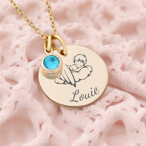 A gold necklace with a circular pendant featuring an engraved name 'Louie' and a birth month stone, presented on a pink textured surface.