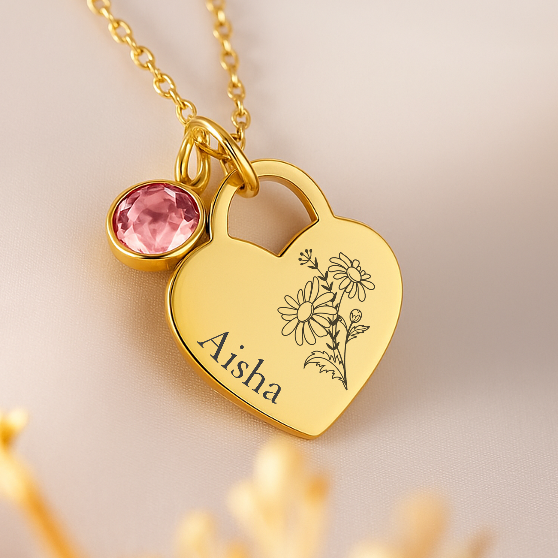 Gold heart-shaped pendant with engraved name and pink gemstone on a light background