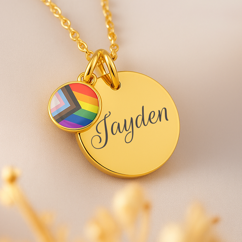 Gold necklace with a rainbow charm and engraved name on a beige background