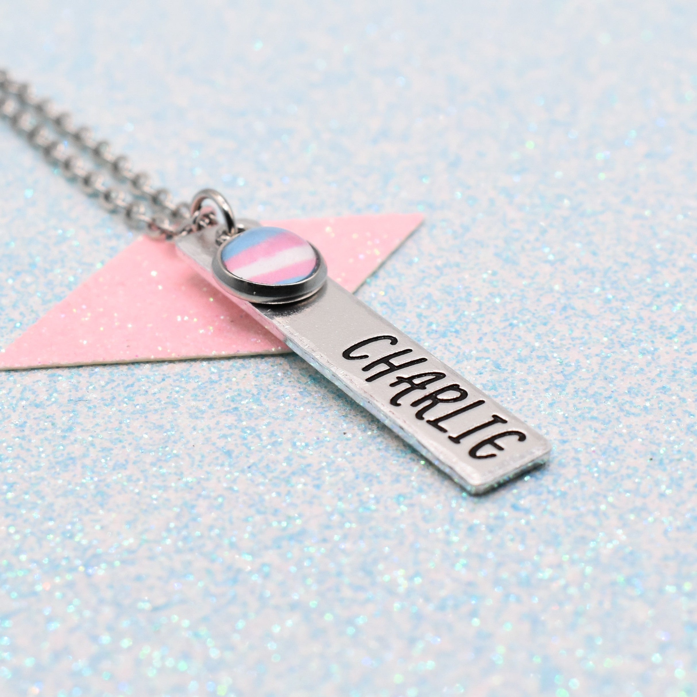 Personalised transgender pride necklace with transgender pride flag and 'personalised' name on a light blue glittery background.