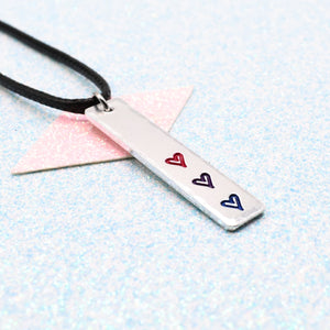 Necklace with a bar pendant on a faux leather cord featuring colourful hearts representing the bisexual pride flag on a light blue background