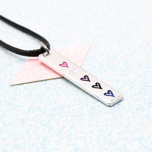 Necklace with a bar pendant on a faux leather cord featuring colourful hearts representing the gender fluid pride flag on a light blue background