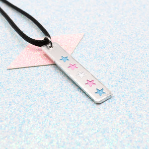 LGBTQ+ Transgender Necklace bar pendant featuring colourful star designs representing the transgender pride flag on a light blue background on a faux leather cord