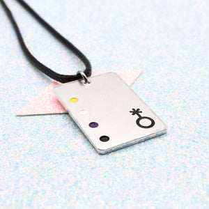 Non Binary Necklace with a rectangular tag featuring a Non Binary symbol and accents on a leather cord displayed on a light blue background