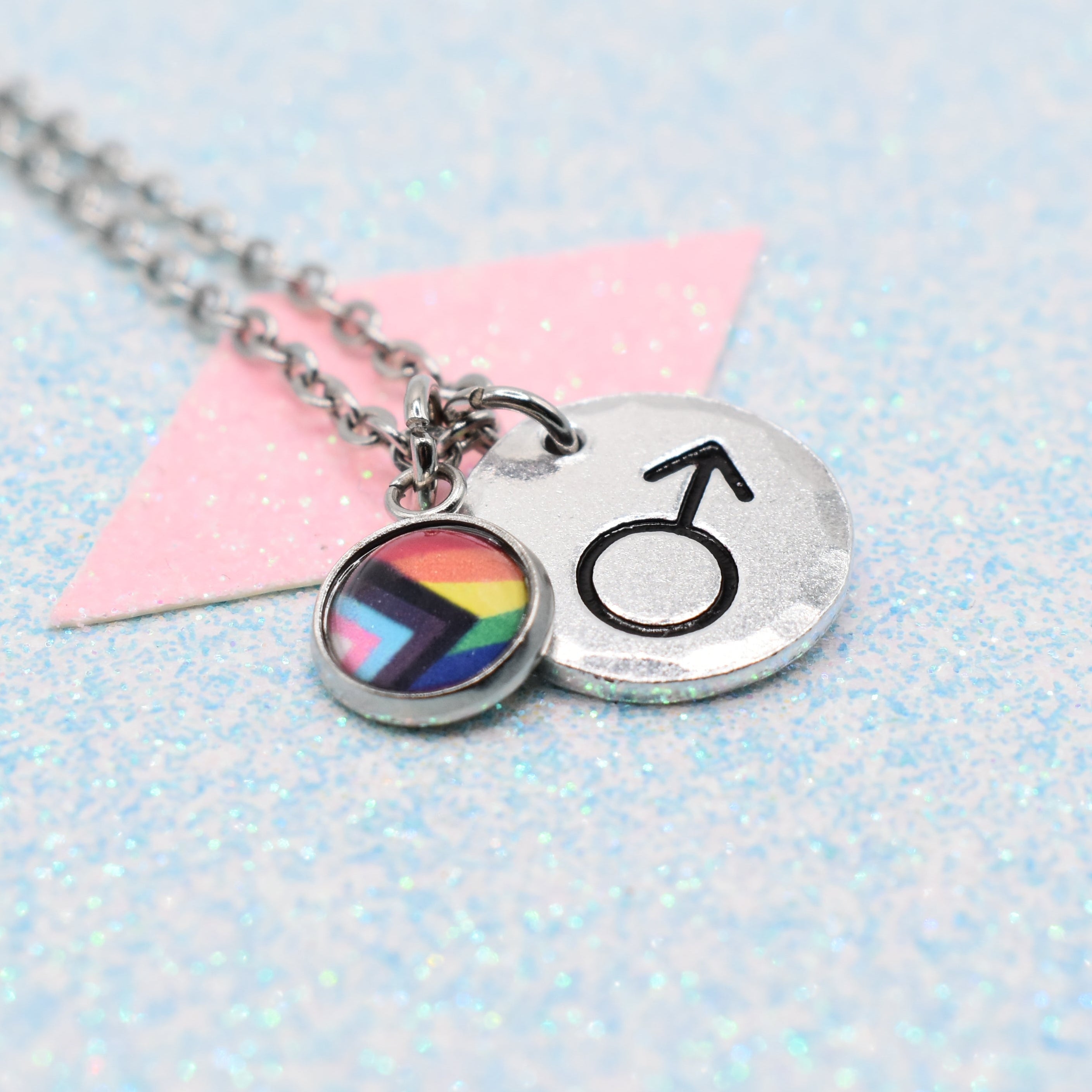 Necklace with a rainbow Pride flag charm and male gender symbol on a light blue background