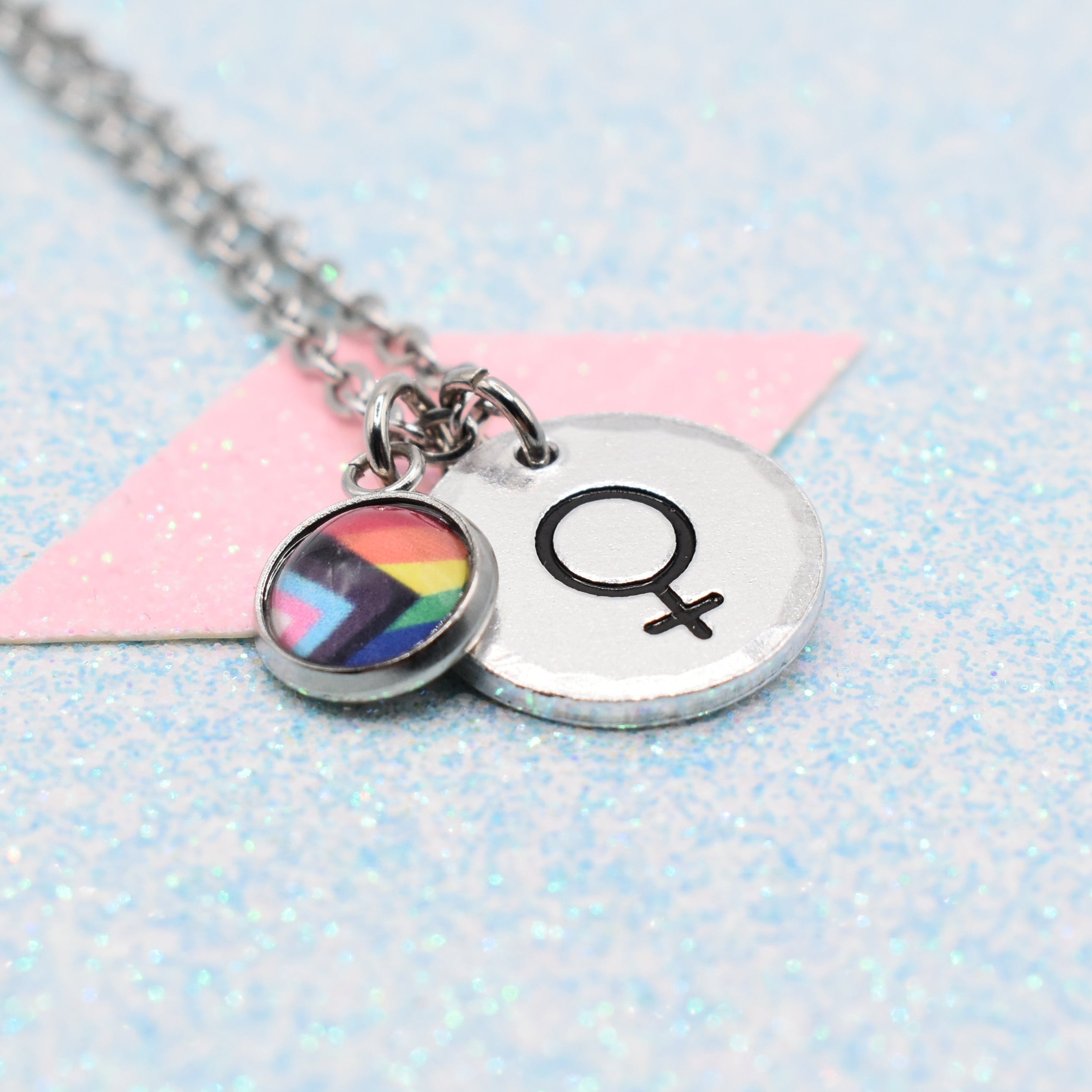 Necklace with a rainbow lgbtq pride flag charm and female gender symbol on a light blue background