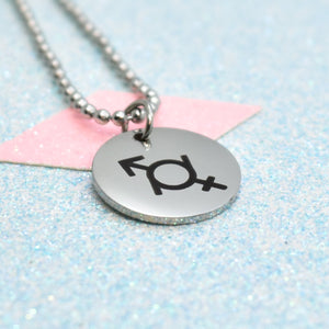 The image shows a silver-coloured necklace with a pendant featuring a black gender fluid emblem. The pendant is round and has a shiny, metallic finish.