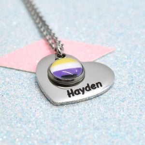A heart-shaped non binary necklace with a pride flag design and the name 'Hayden' on it, attached to a silver-coloured chain.