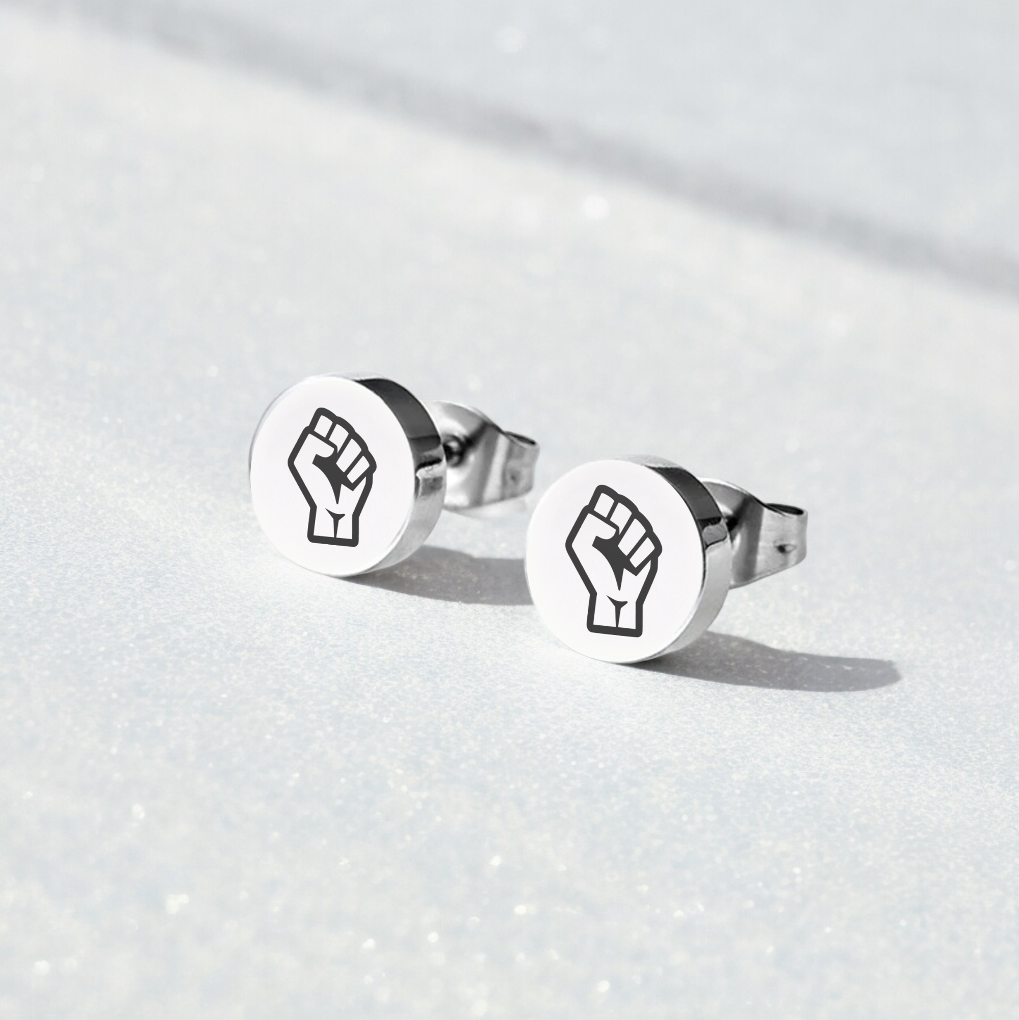 Pair of earring studs with Resist Fist Logo on blue background