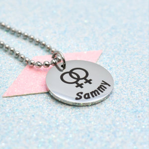 A lesbian pride necklace with a silver emblem and the name 'Sammy' on it, attached to a pink tag.