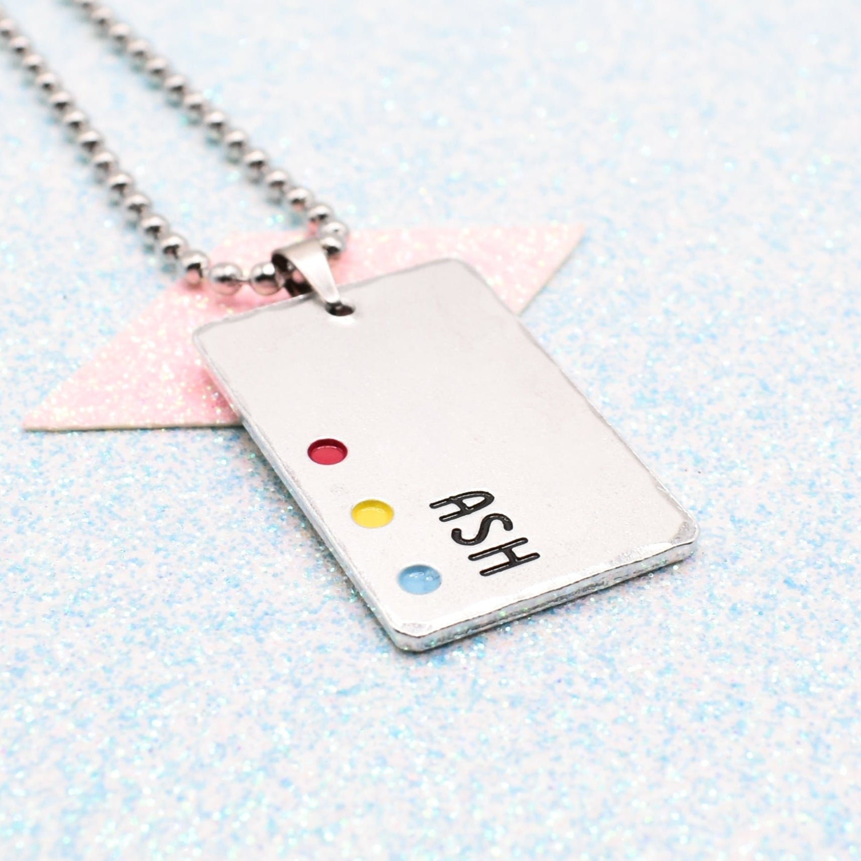 Customisable LGBTQ+ Pride Necklace featuring enamels of the pansexual pride flag and a personalised name mounted on a ball chain displayed on a blue background