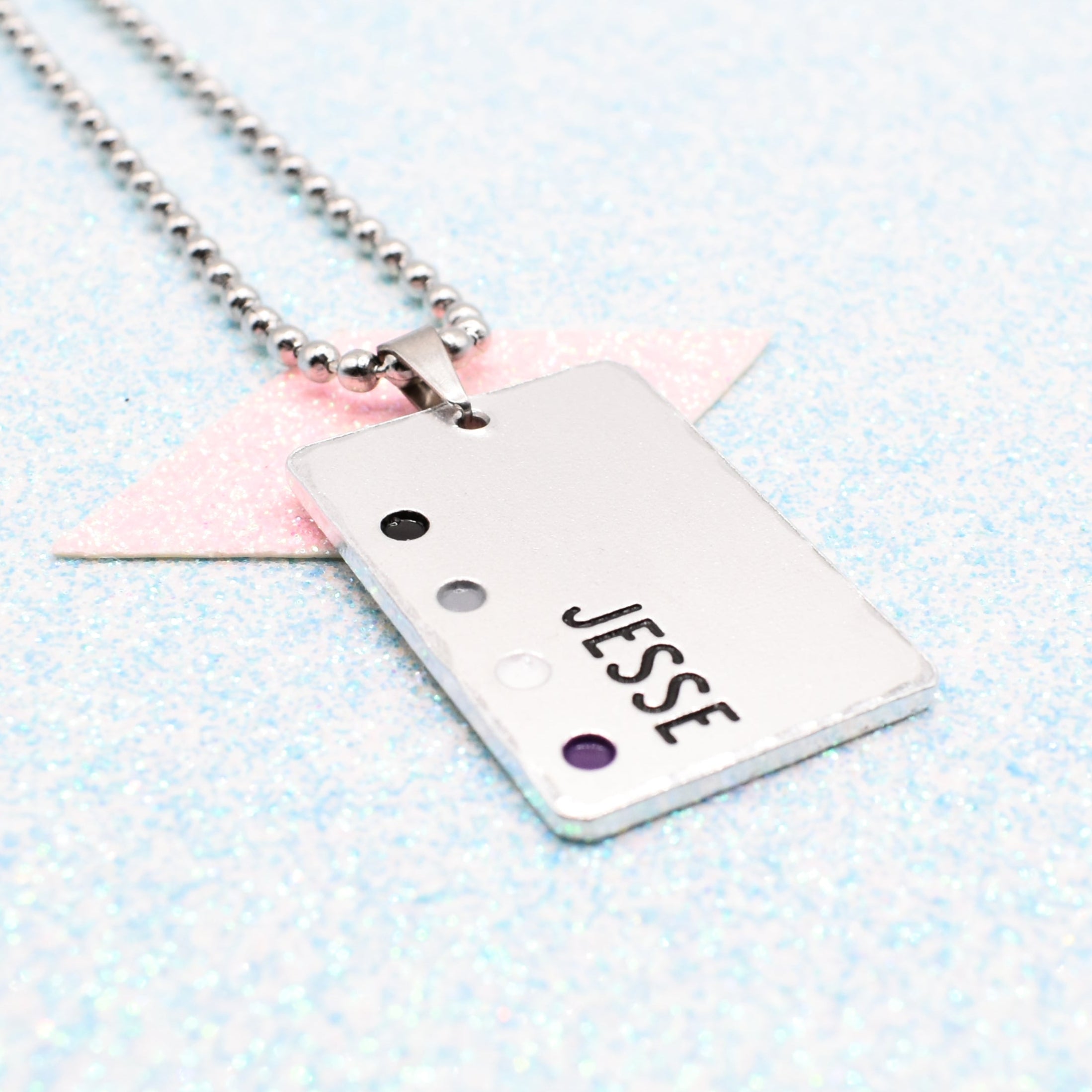 Customisable LGBTQ+ Pride Necklace featuring enamels of the Asexual pride flag and a personalised name mounted on a ball chain displayed on a blue background
