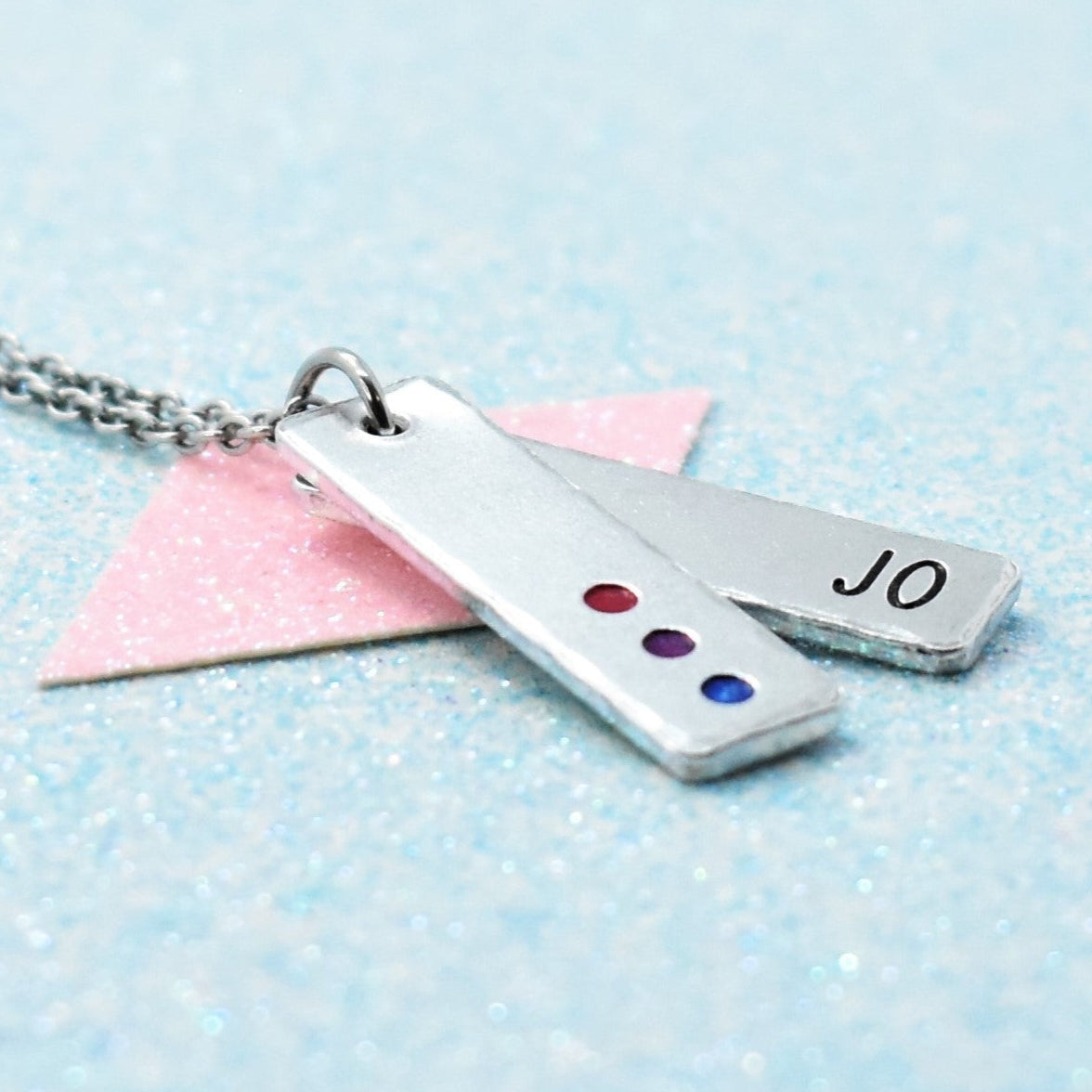 A minimalist personalised bisexual pride necklace with an enamelled pendant in the colors of the bisexual pride flag, attached to a cable chain. The pendant features the name 'Jo' with a date '08.
