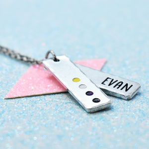 Customisable lgbtq pride pendant with Non Binary pride colours and 'EVAN' engraved, on a light blue background.