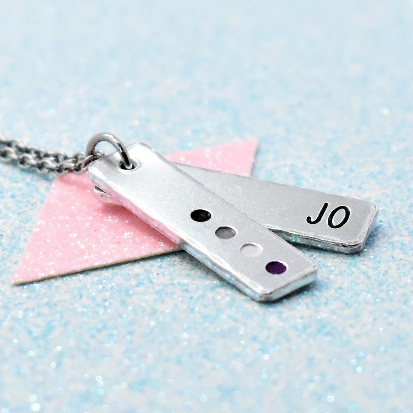 A personalised asexual pride necklace with a minimalist design, featuring a silver-colored pendant enamelled with the flag colors and the name 'Jo'.