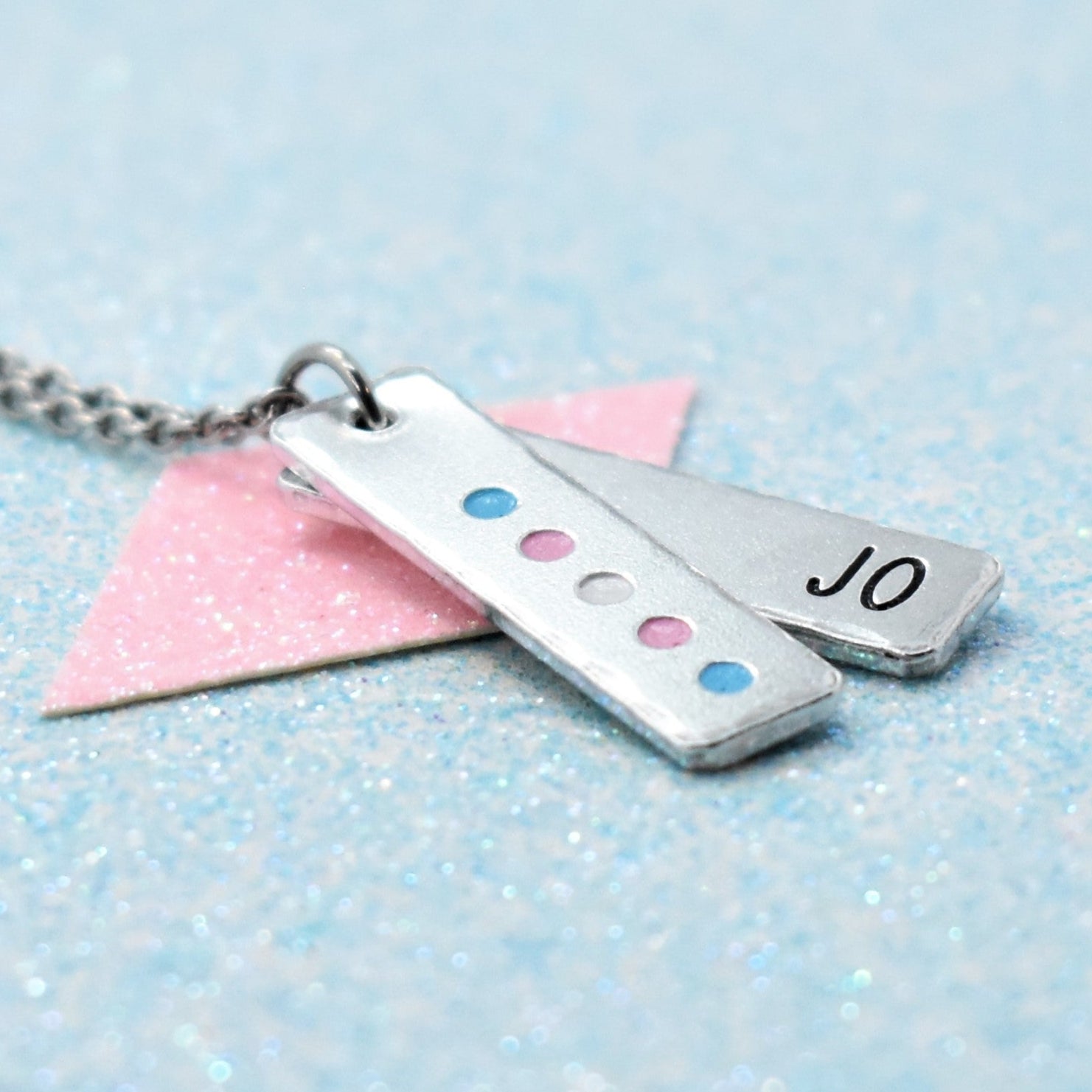 A minimalist, personalised transgender pride necklace with an enamelled pendant in the colors of the transgender pride flag, attached to a metal chain.