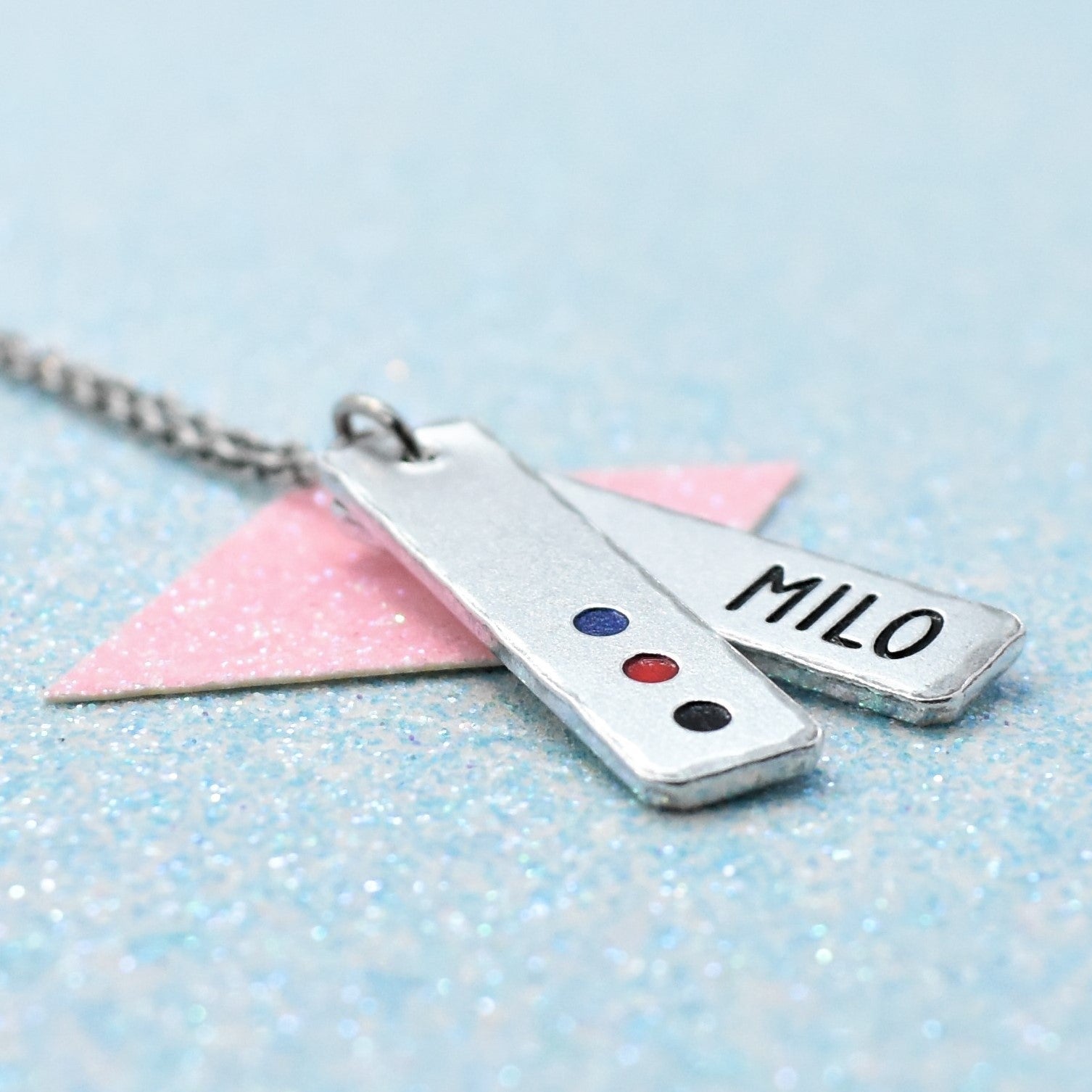 Customisable lgbtq pride pendant with polyamory pride colours and 'MILO' engraved, on a light blue background.