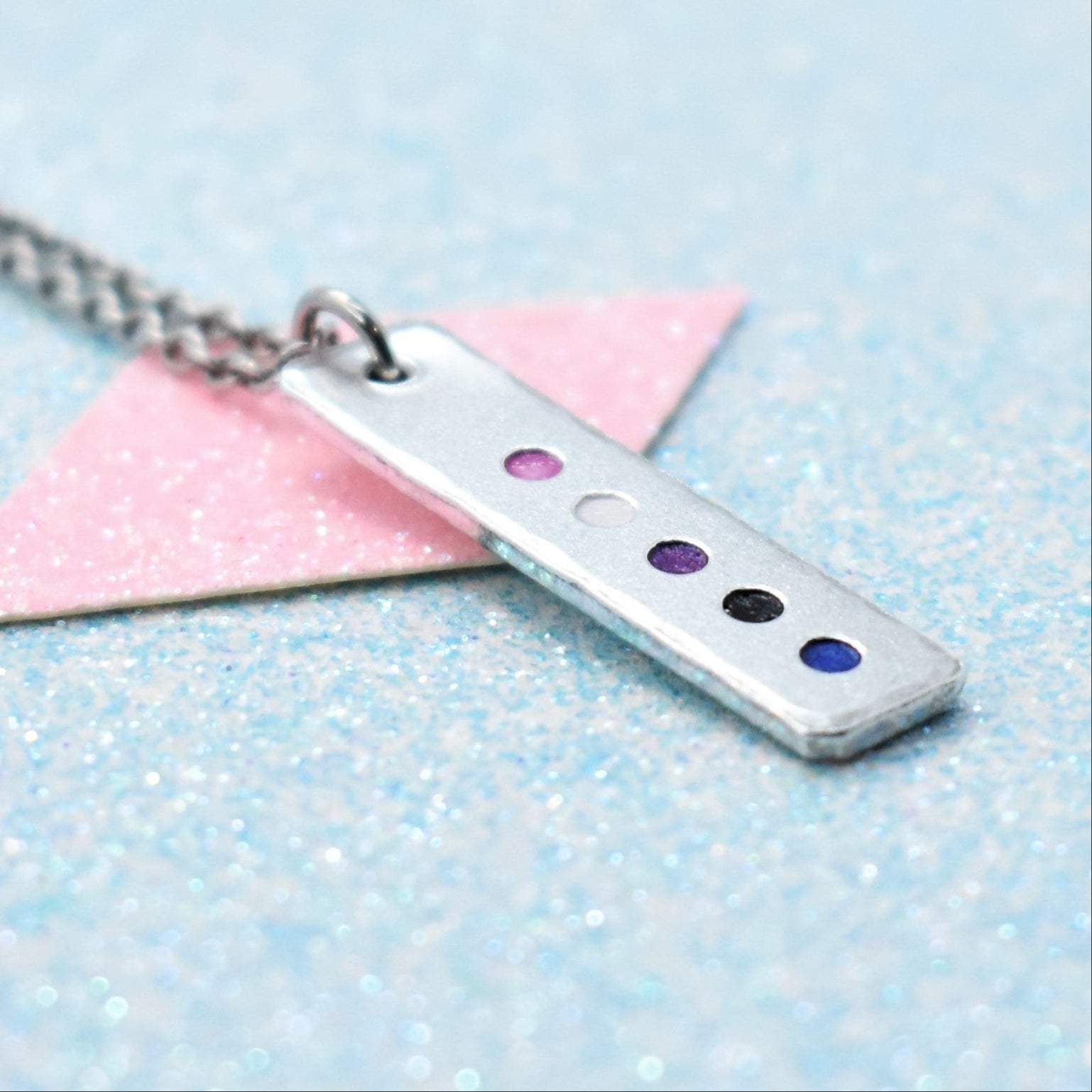 A minimalist pride necklace with a geometric shaped pendant featuring the gender fluid flag colours, attached to a silver-coloured chain.