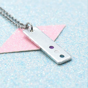 A minimalist pride necklace with a geometric shaped pendant featuring the gender queer flag colours, attached to a silver-coloured chain.