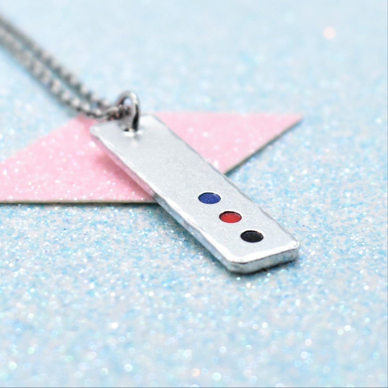 A minimalist polyamorous pride necklace with a geometric shaped pendant featuring the polyamory flag colours, attached to a silver-coloured chain.