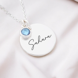A personalized necklace with a birthstone, the pendant is engraved with the name 'Sahara' and attached to a silver cable chain with a lobster clasp.