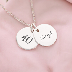 A personalized milestone necklace with two round pendants on a chain, one with the number 40 and the other with the name Lucy.