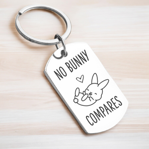 A key ring with a rectangular tag featuring text and a cartoon rabbit design, on a wooden surface.