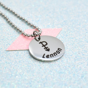 A pansexual necklace with a silver emblem and the name 'Lennon' on it, attached to a pink tag.