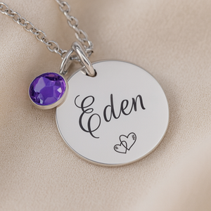 Silver necklace with a round pendant featuring the name 'Eden' and a purple gemstone on a beige background.
