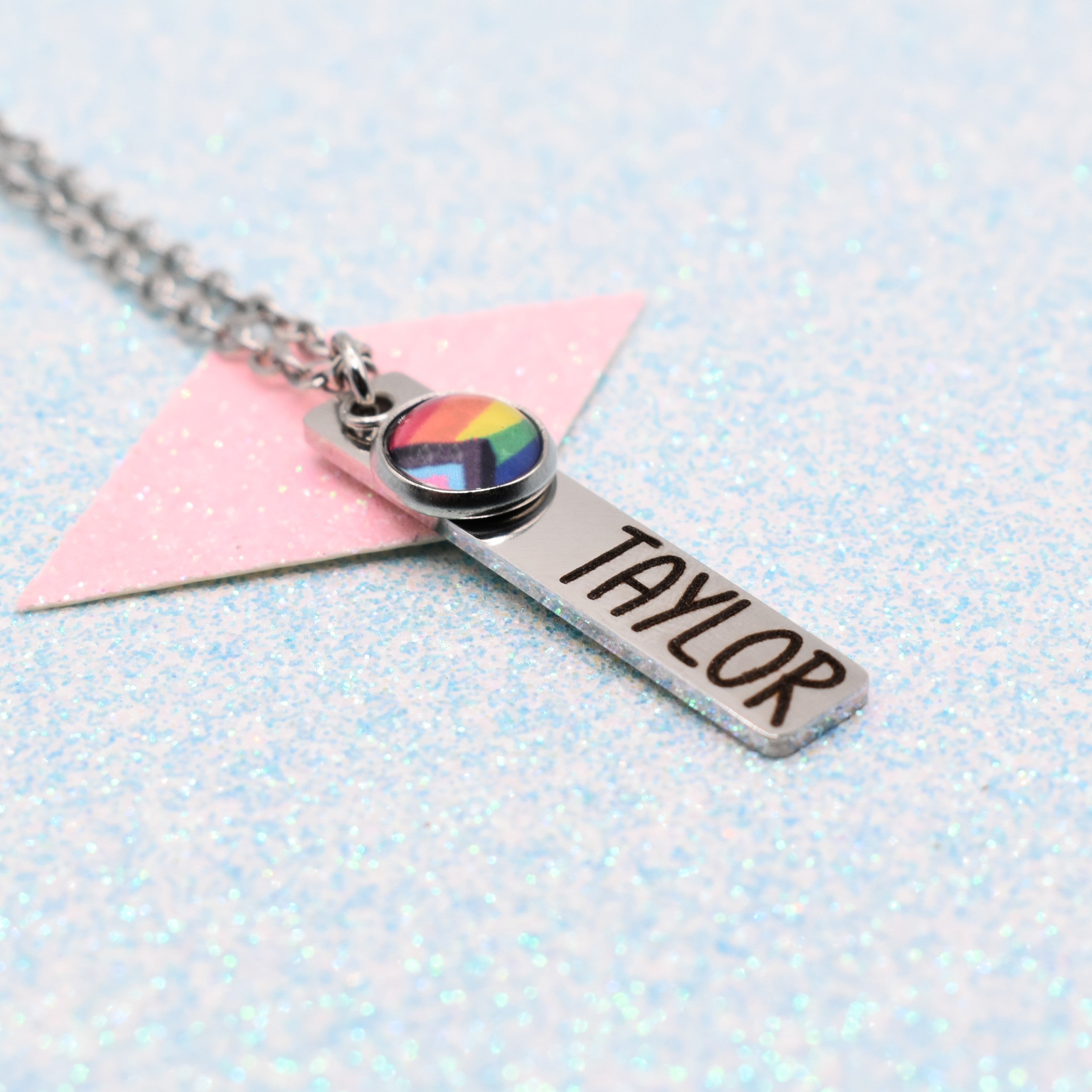 Necklace with a name tag and rainbow pride flag pendant on a light blue background