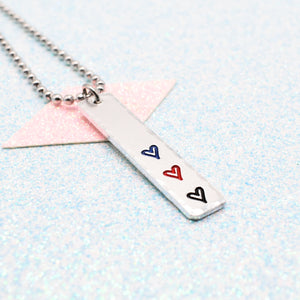 Necklace with a bar pendant on a ball chain featuring colourful hearts representing the polyamory pride flag on a light blue background