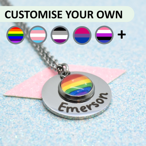 A custom pride necklace with a pride pendant featuring the pride flag symbol, and a personalised name written on the pendant. The necklace is displayed on a blue background with a shimmering surface.
