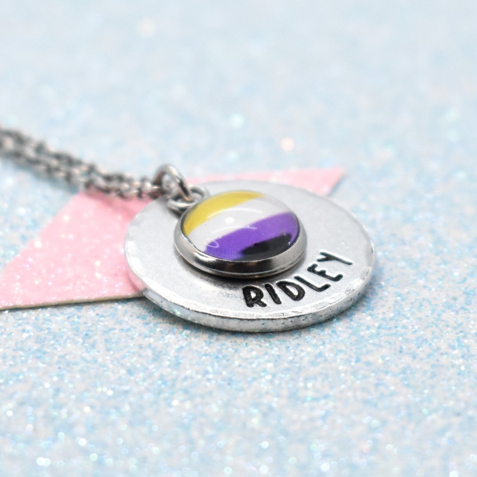 Pride Necklace with a round pendant featuring a non binary flag design and a hand-stamped name on a glittery background.