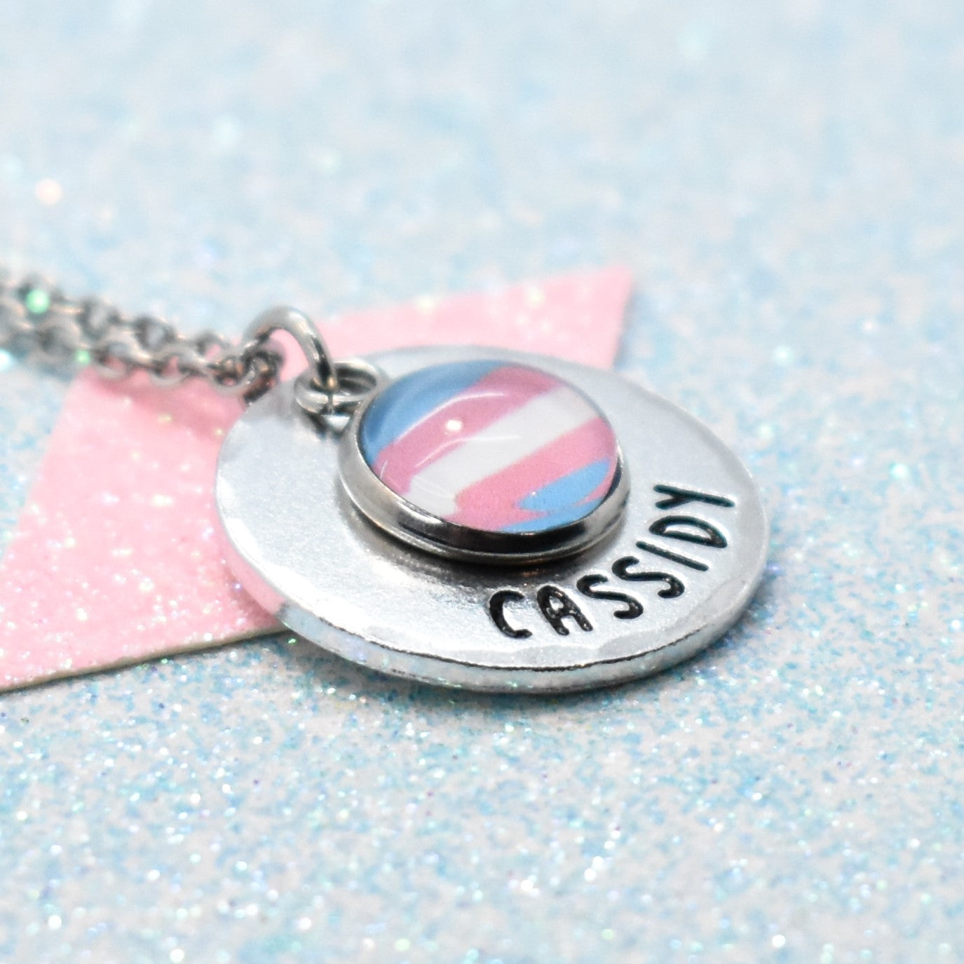 LGBTQ Necklace with a transgender flag charm and engraved name 'Personalised' on a glittery background
