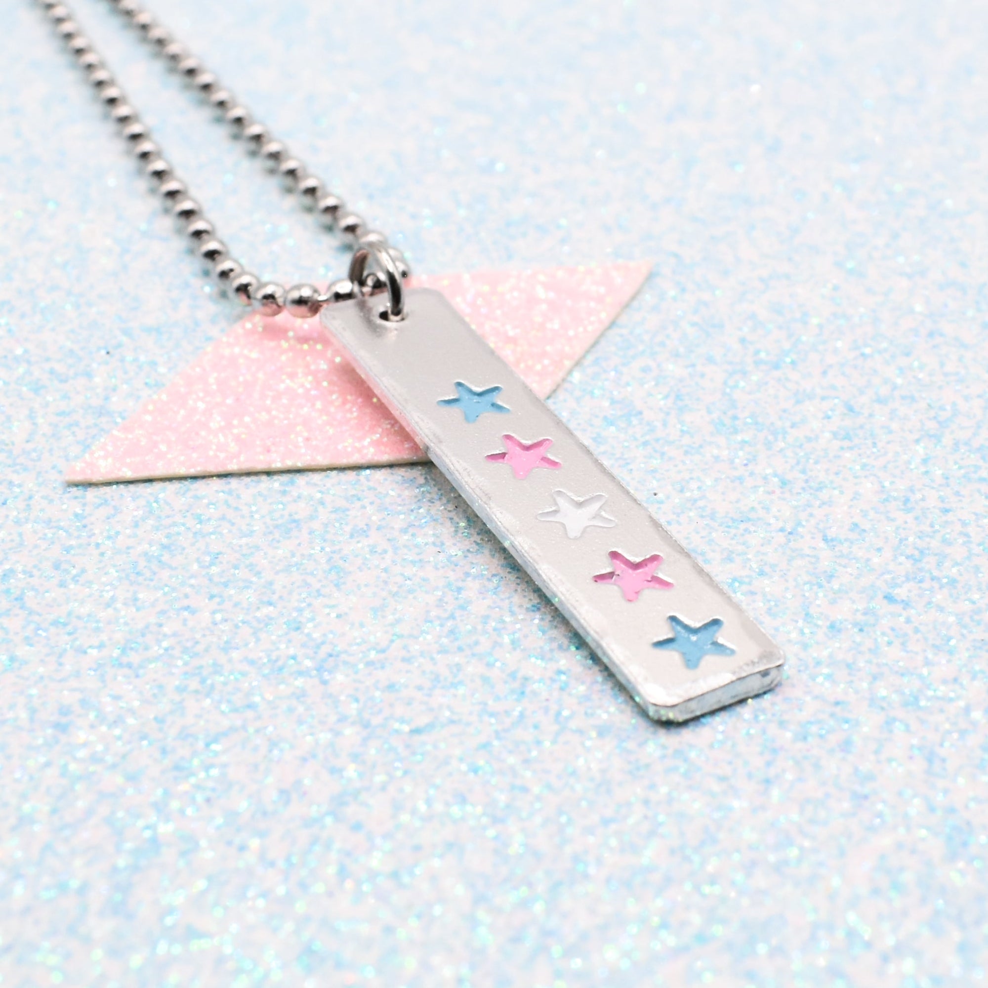 LGBTQ+ Transgender Necklace bar pendant featuring colourful star designs representing the transgender pride flag on a light blue background on a Ball Chain