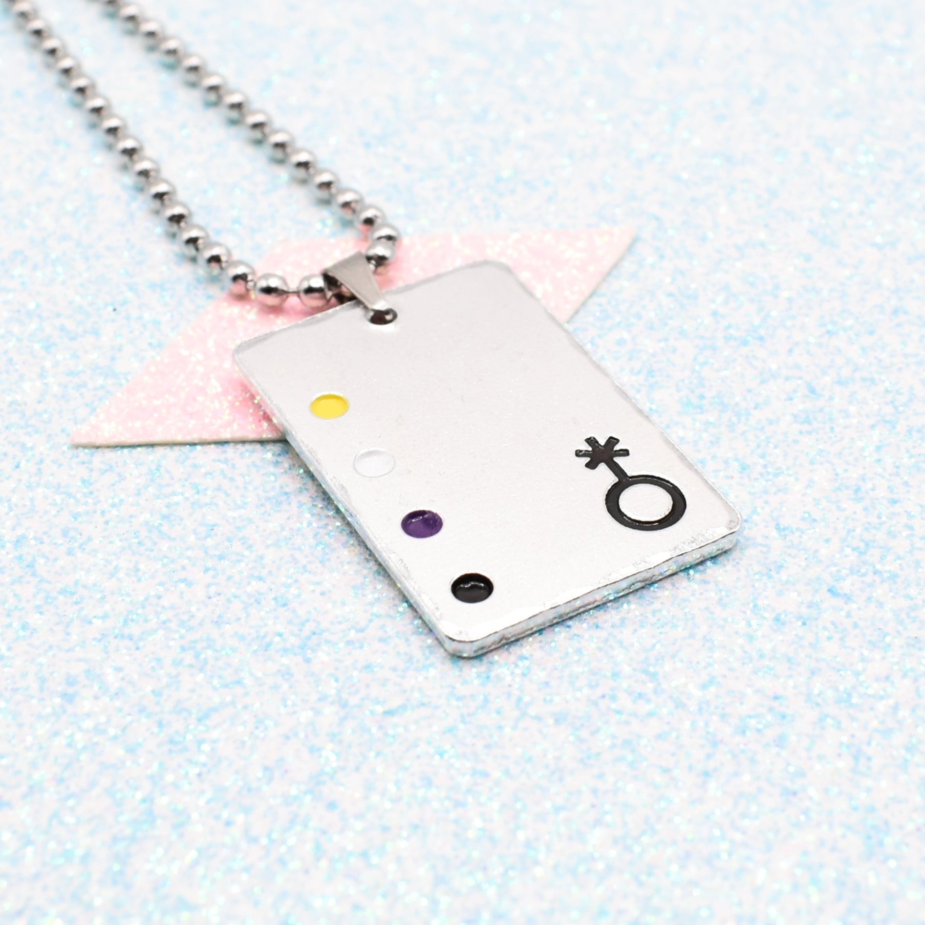 Non Binary Necklace with a rectangular tag featuring a Non Binary symbol and accents on a ball chain displayed on a light blue background